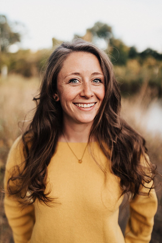 a smiling person in a yellow sweater standing in front of scenery
